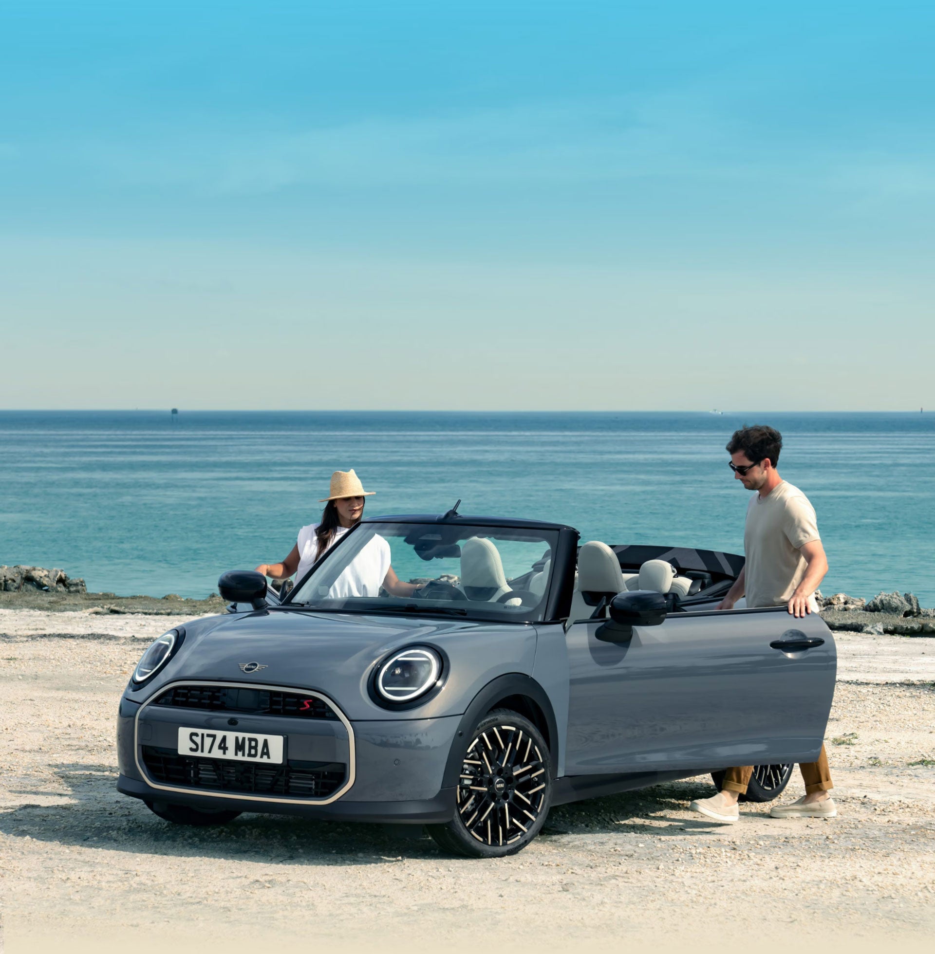 Convertible parked on a beach with two drivers getting into it.